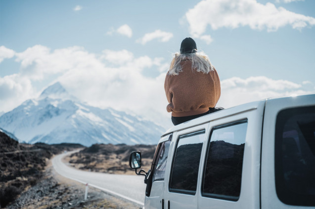 Vanlife Neuseeland. Frau sitzt auf Van mit Sicht auf den Mount Cook in Neuseeland